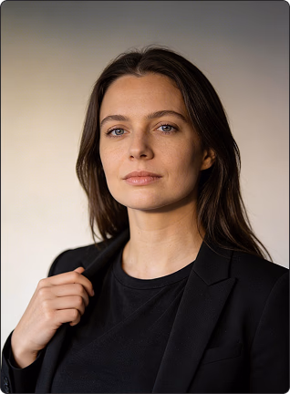 Woman with long brown hair in black blazer and shirt looking seriously at the camera.