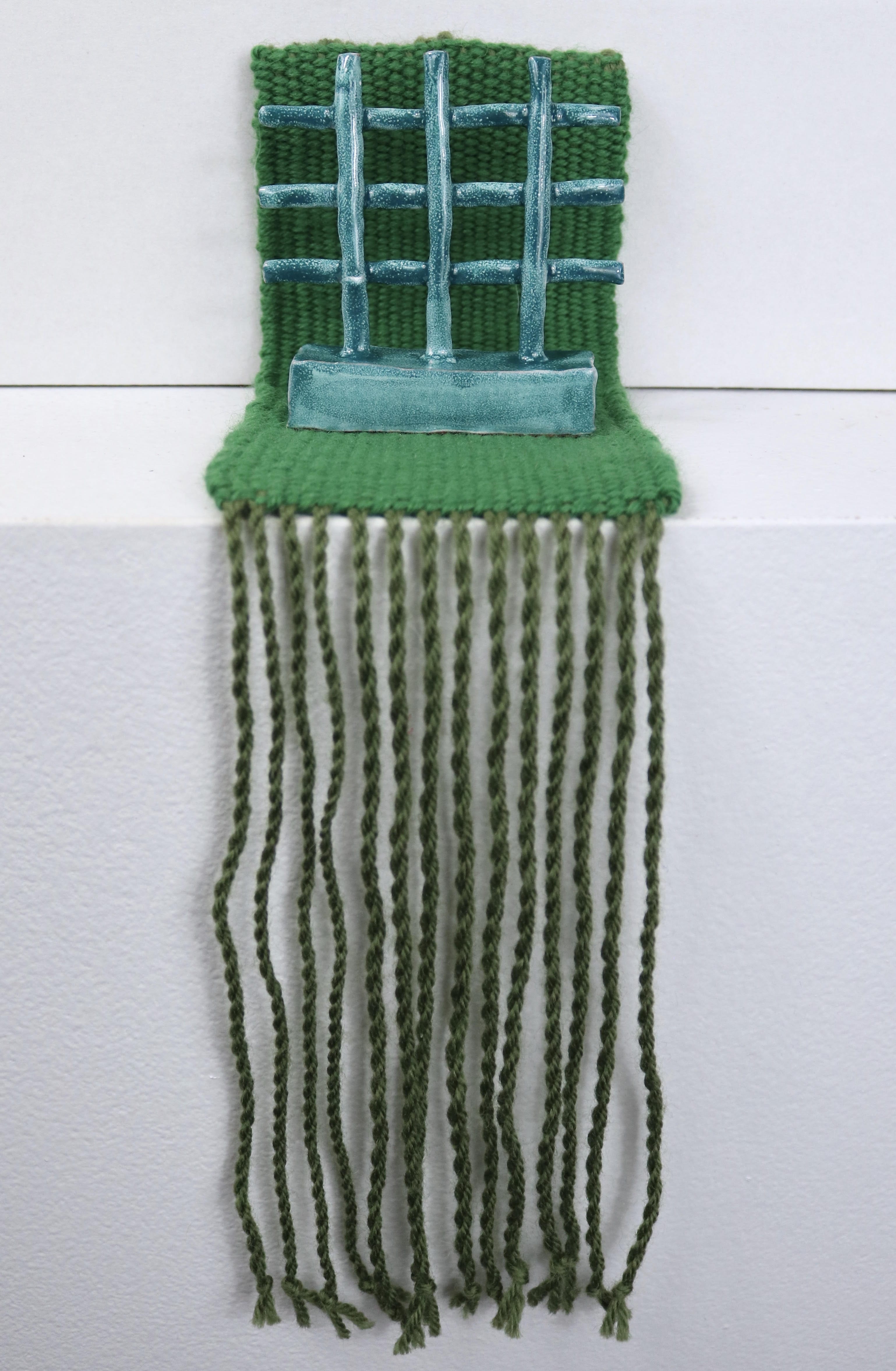 Artwork containing blue-green ceramic lattice piece atop a green woven textile.