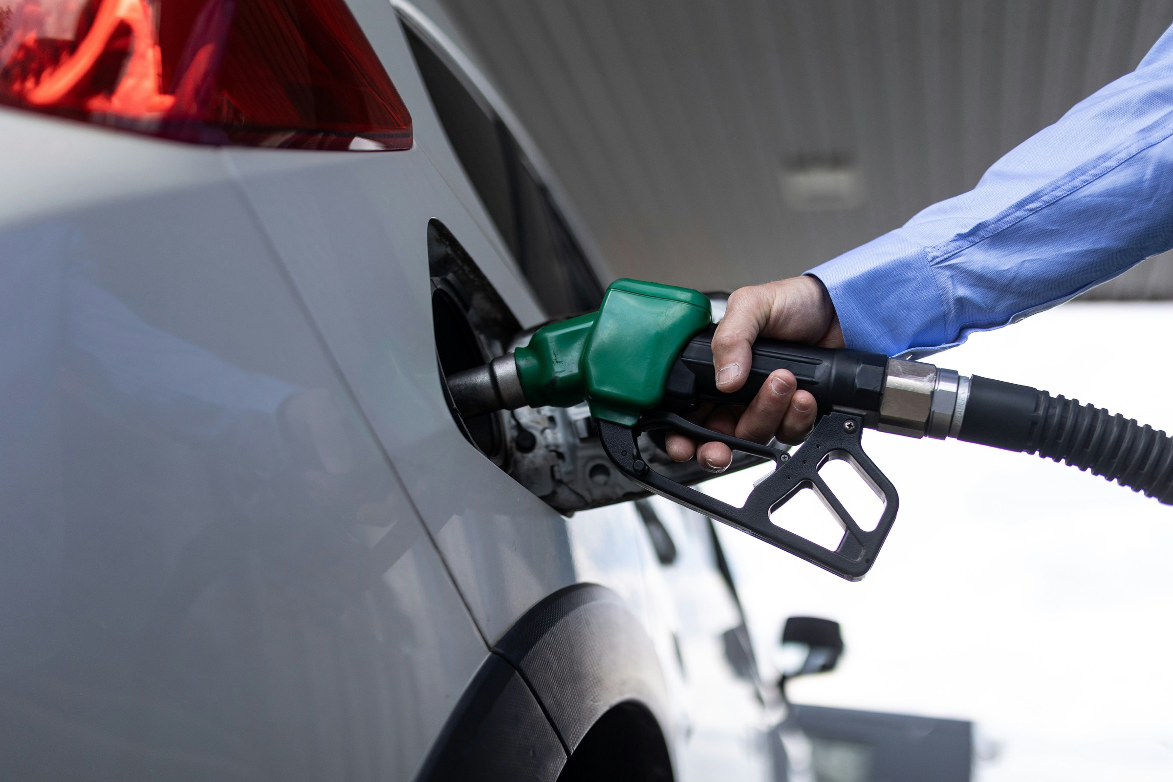 A green fuel nozzle held in a car's filler neck during refuelling
