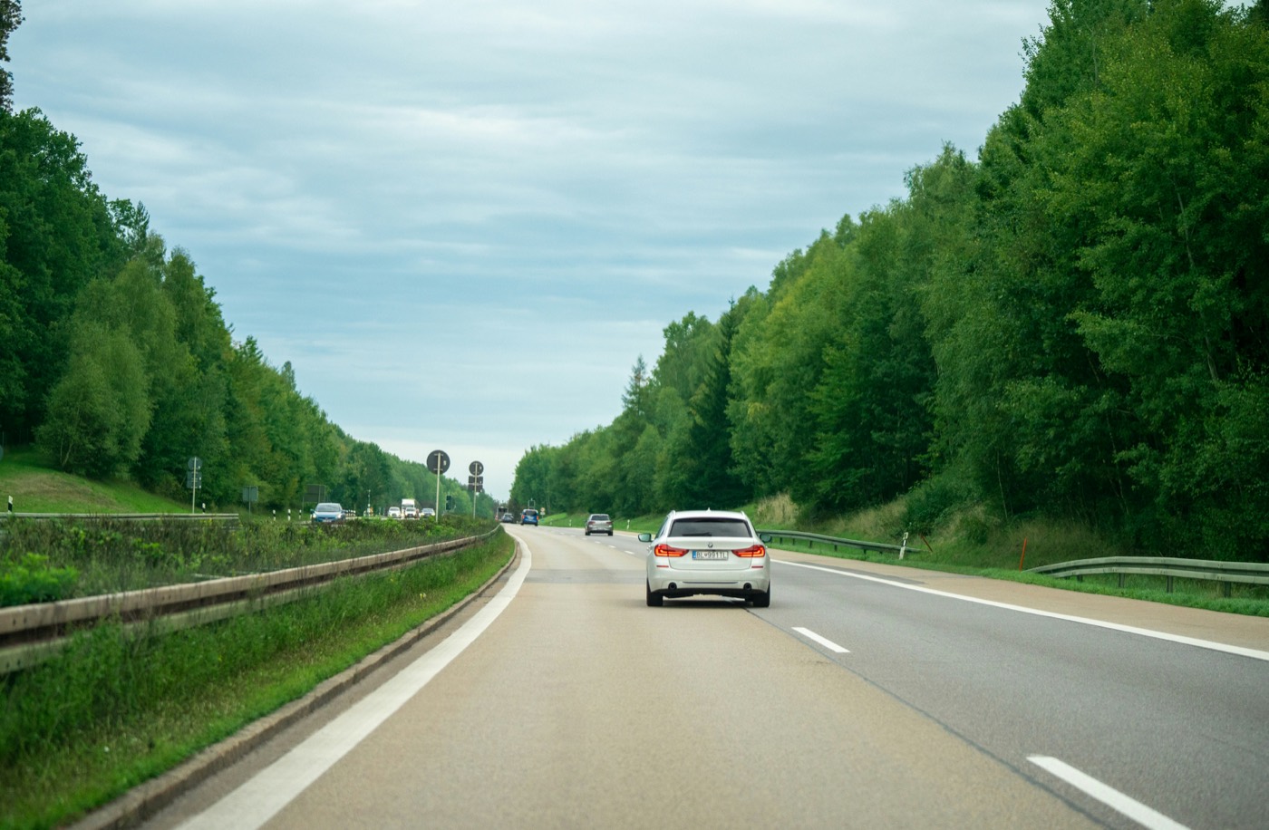 A car on an open highway lined with trees, seen from the vehicle behind