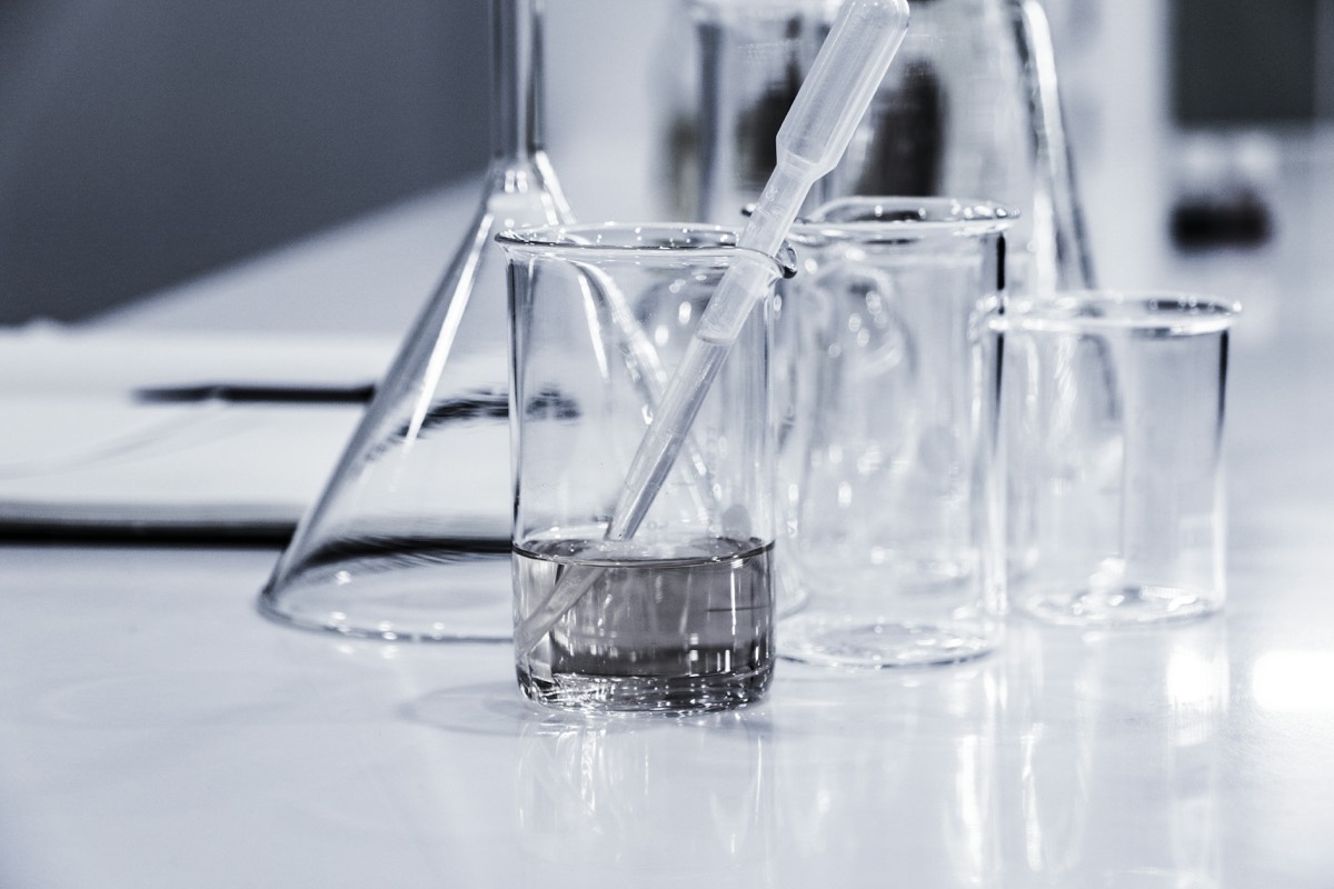 A pipette resting in a laboratory beaker beside empty glassware
