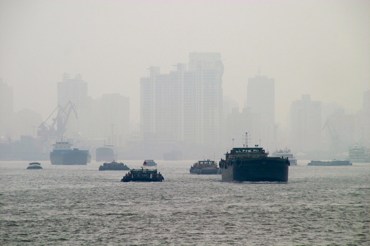 A city skyline and river barges almost lost in thick grey haze.