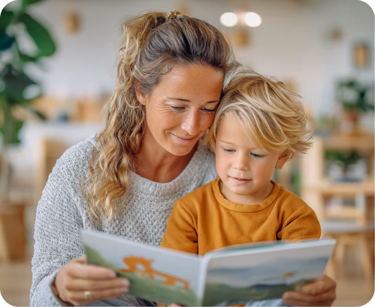 Woman reading a book with a young boy in a cozy indoor setting.