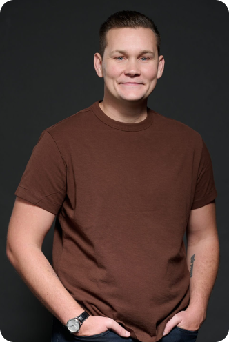 Am image of a man who is Calvin Coyles wearing a brown shirt with hands in pocket smiling at the camera. 