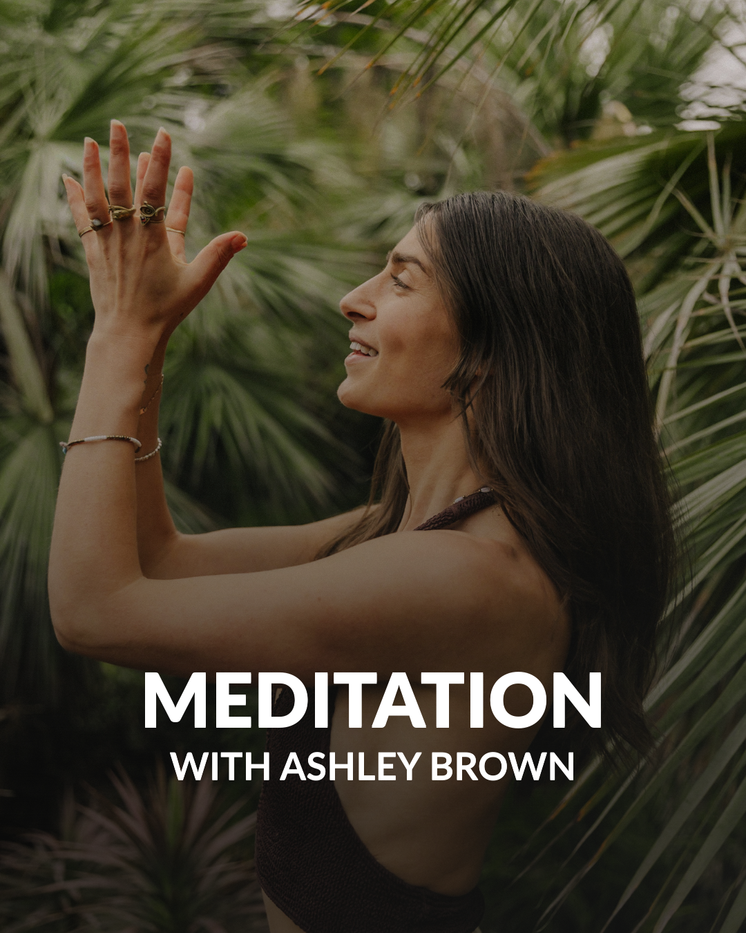 Smiling woman with long dark hair and rings on her fingers with palms pressed together, surrounded by green tropical plants, with text 'Meditation with Ashley Brown'.
