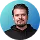 Portrait of a man with short hair and beard wearing a black shirt against a blue background.