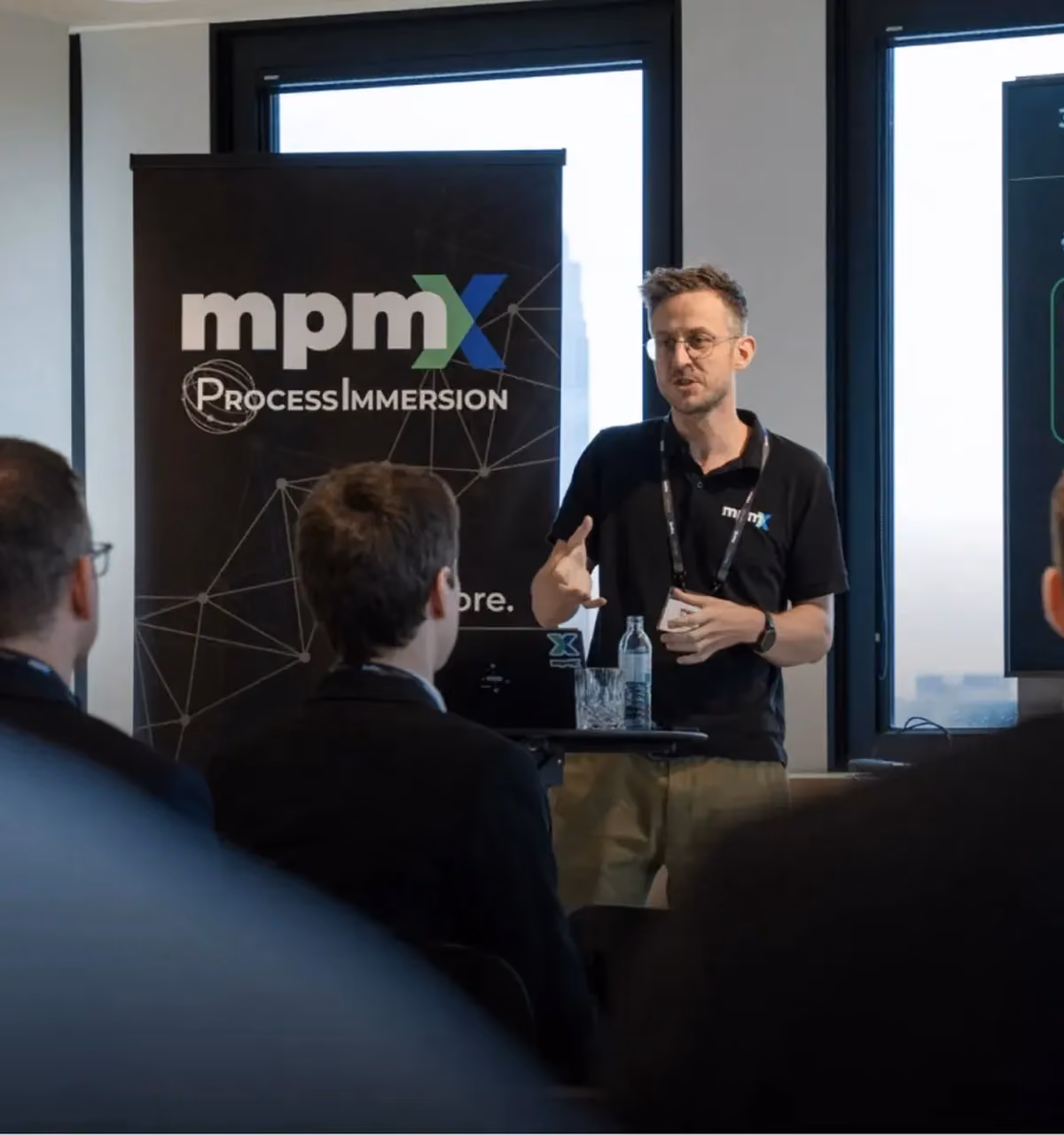 Man in mpmX shirt giving a presentation to an audience in a conference room.