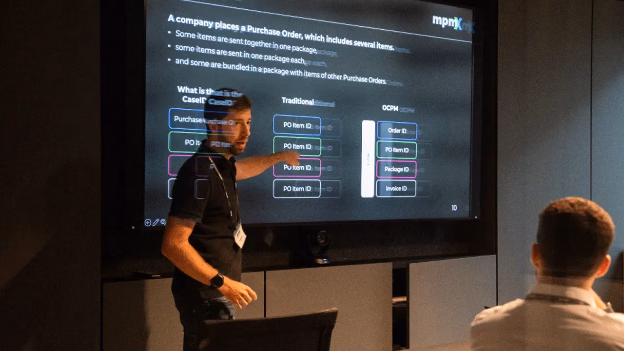 Man in black shirt presenting purchase order workflow on screen to seated audience in conference room.