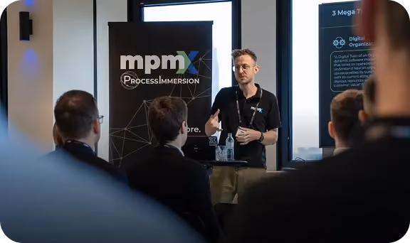 Man giving a presentation in front of an audience with an MPM Process Immersion banner.