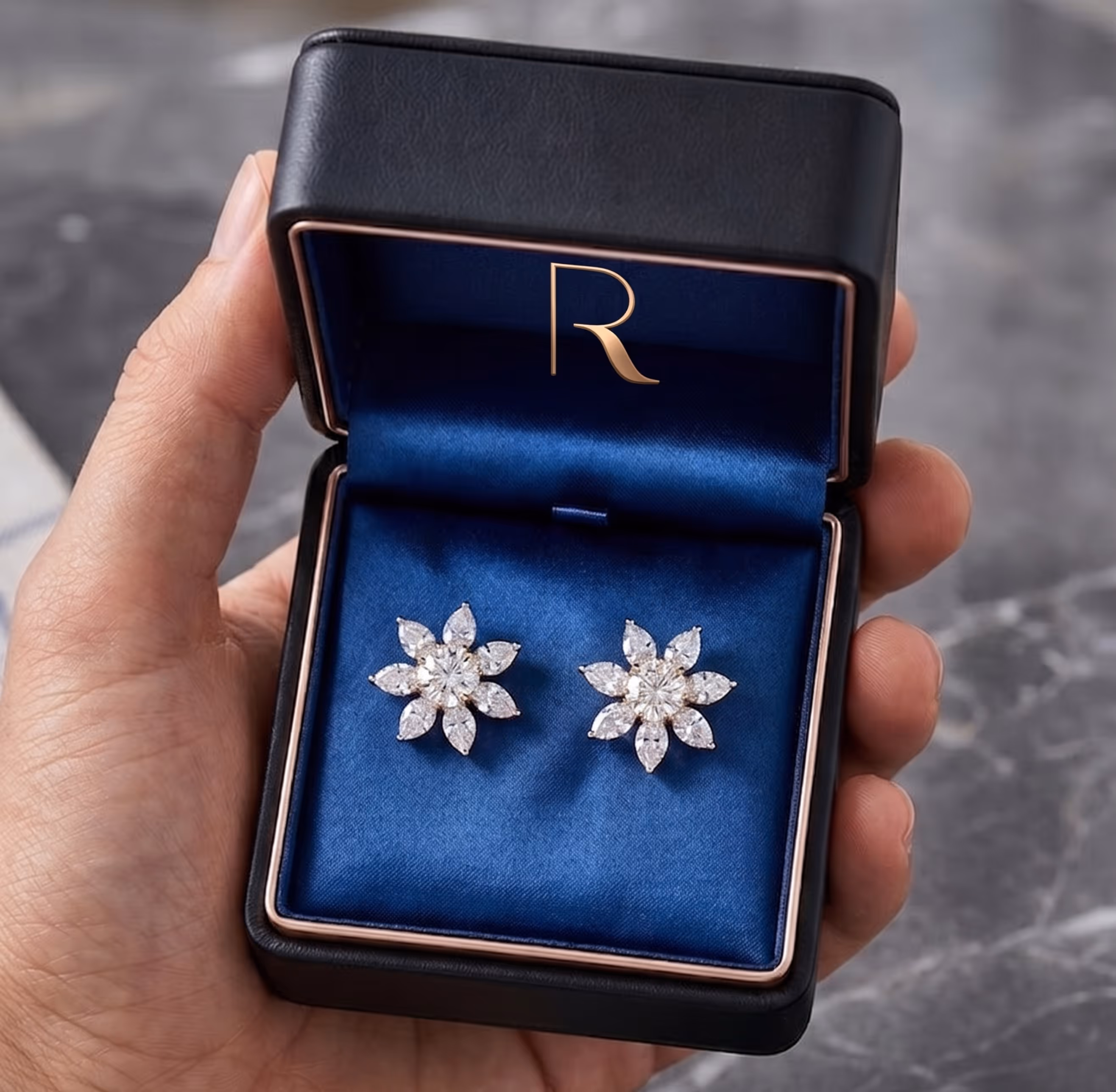 Hand holding open black jewelry box with blue velvet interior containing a pair of flower-shaped diamond earrings.