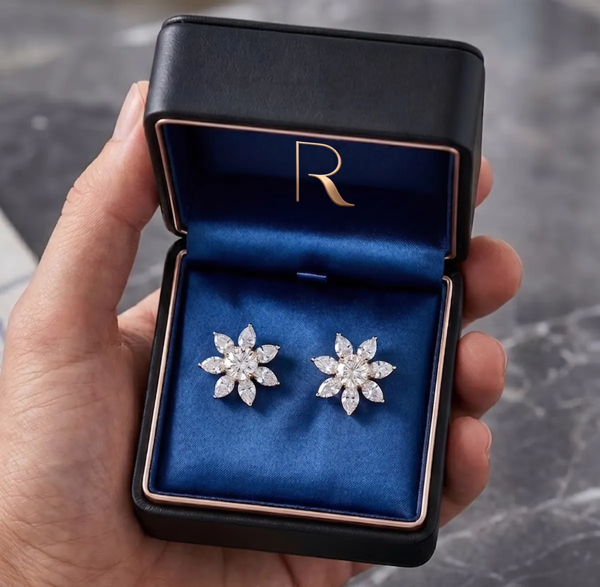 Hand holding open black jewelry box with blue velvet interior containing a pair of flower-shaped diamond earrings.