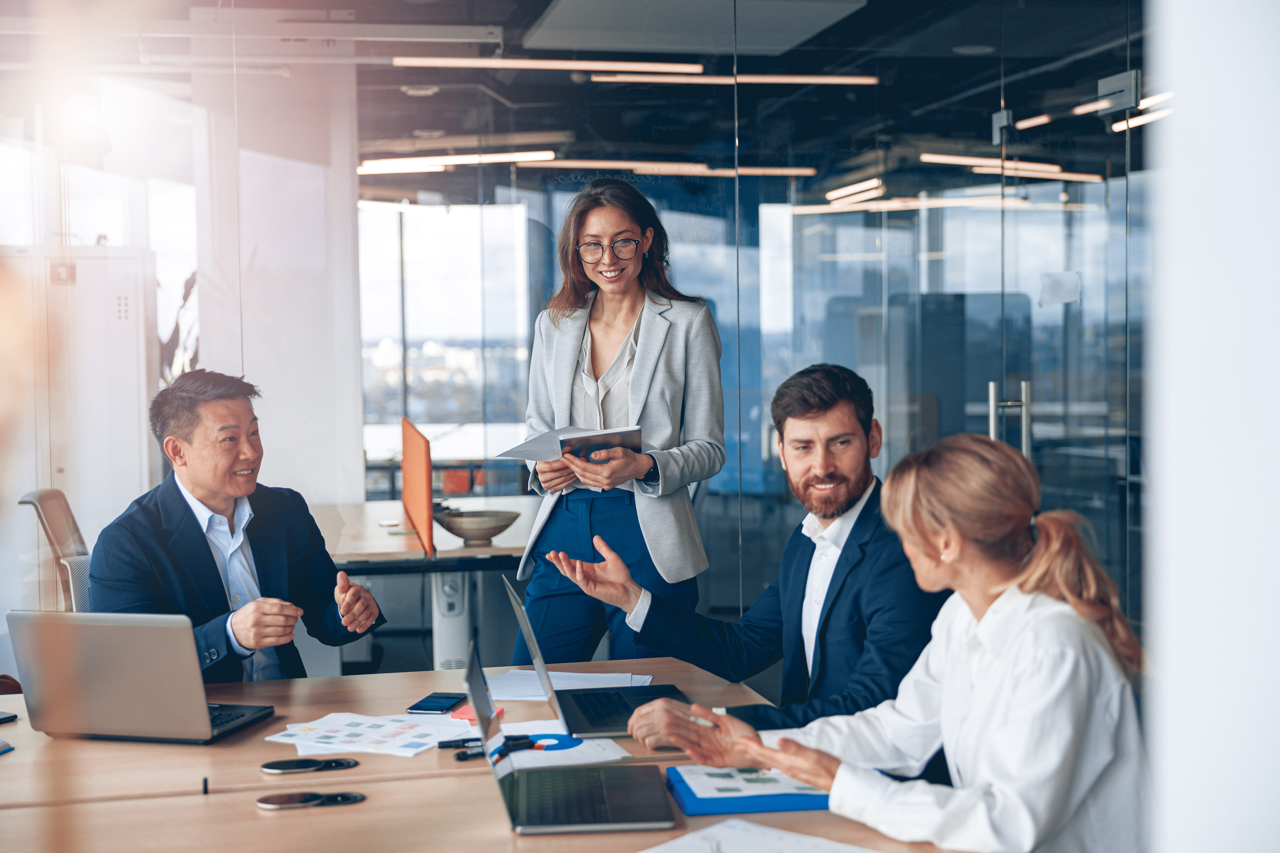 Vier collega's in een moderne vergaderruimte hebben een positieve bespreking met laptops en documenten op tafel.