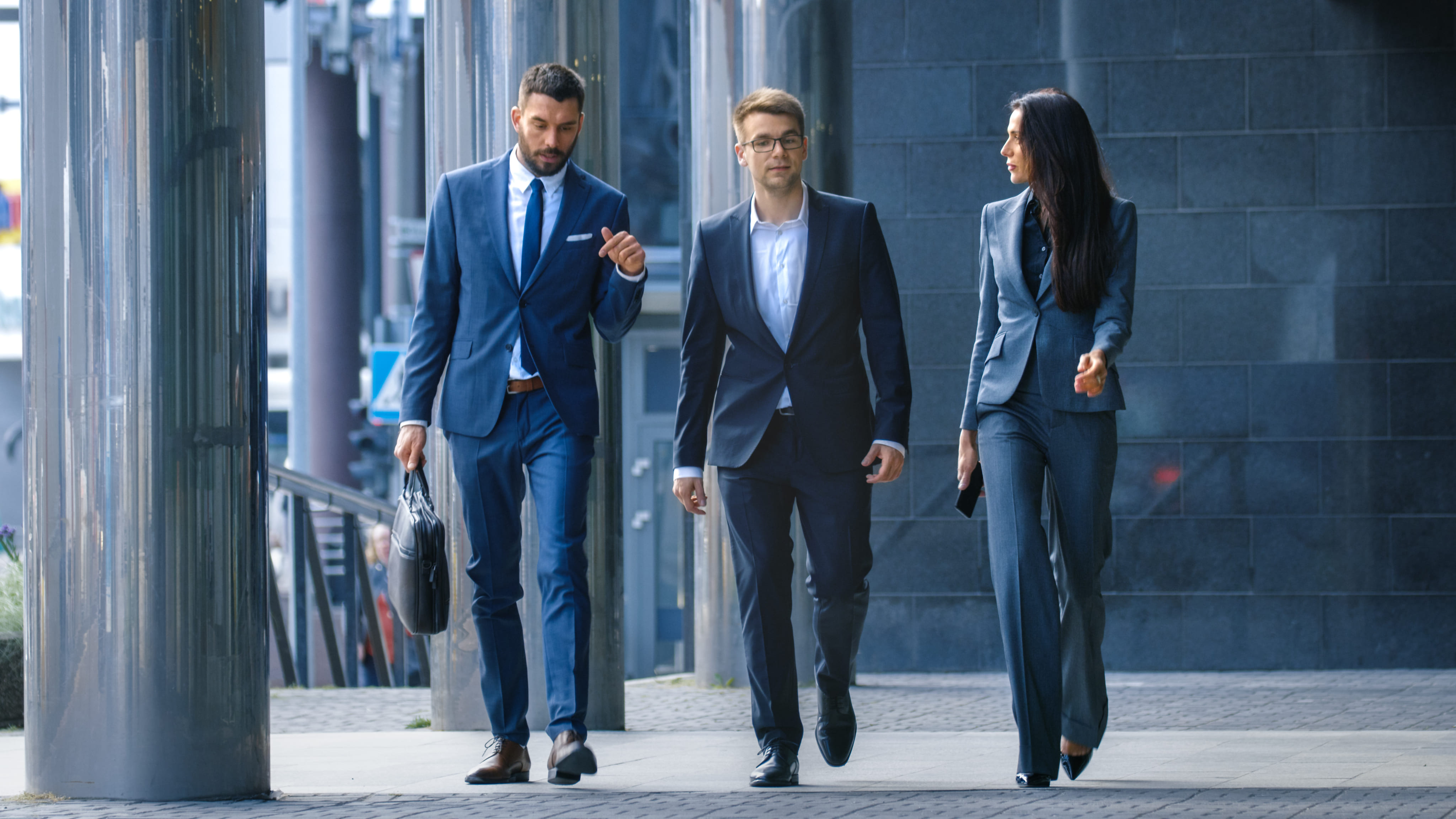 Drie zakelijke professionals in pakken lopen en praten in een stedelijke omgeving.
