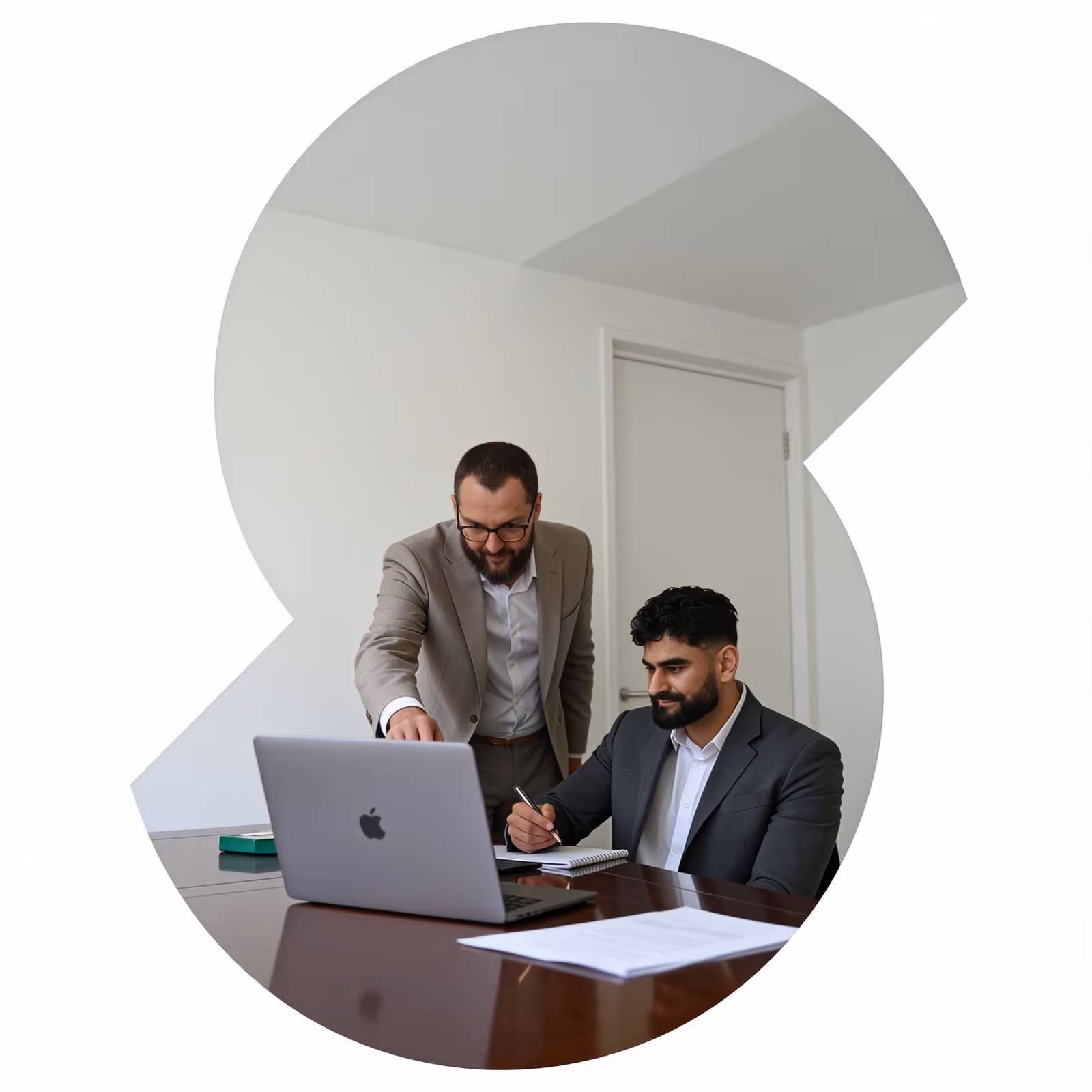 Twee zakenmannen die samen op een laptop werken in een kantoorruimte met een notitieboekje.