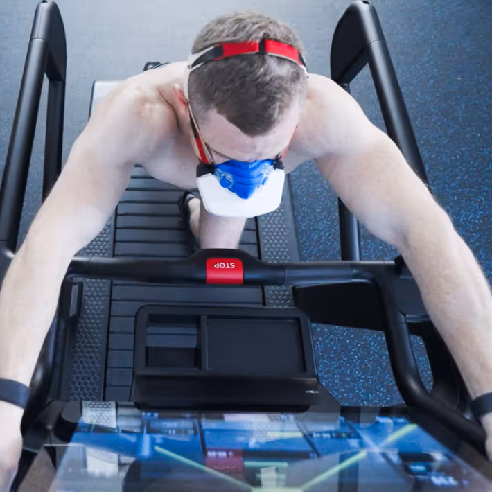 Top view of a shirtless man wearing an oxygen mask exercising on a treadmill.