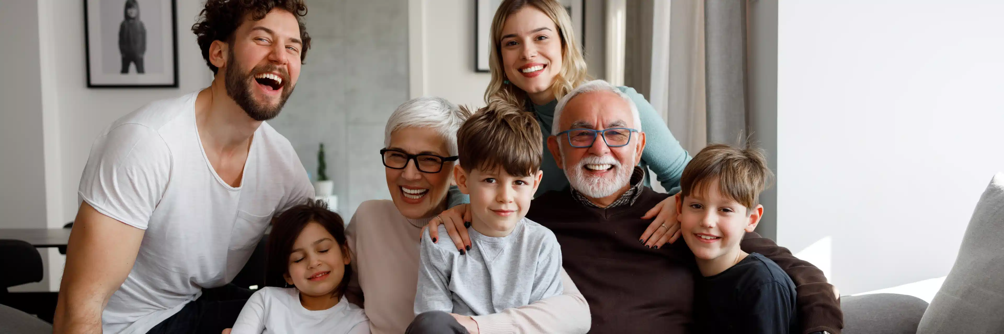 Drei Generationen einer Familie lachen und sitzen eng zusammen auf einer Wohnzimmereinrichtung.
