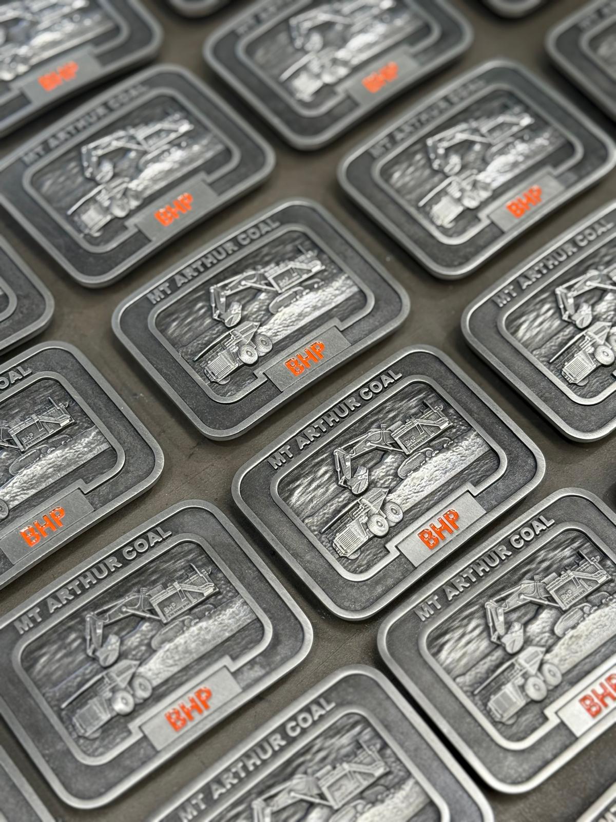 Custom pewter recognition buckles manufactured for Mt Arthur Coal with excavator and haul truck artwork