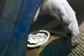 Gloved hand handling finished metal recognition buckle during production