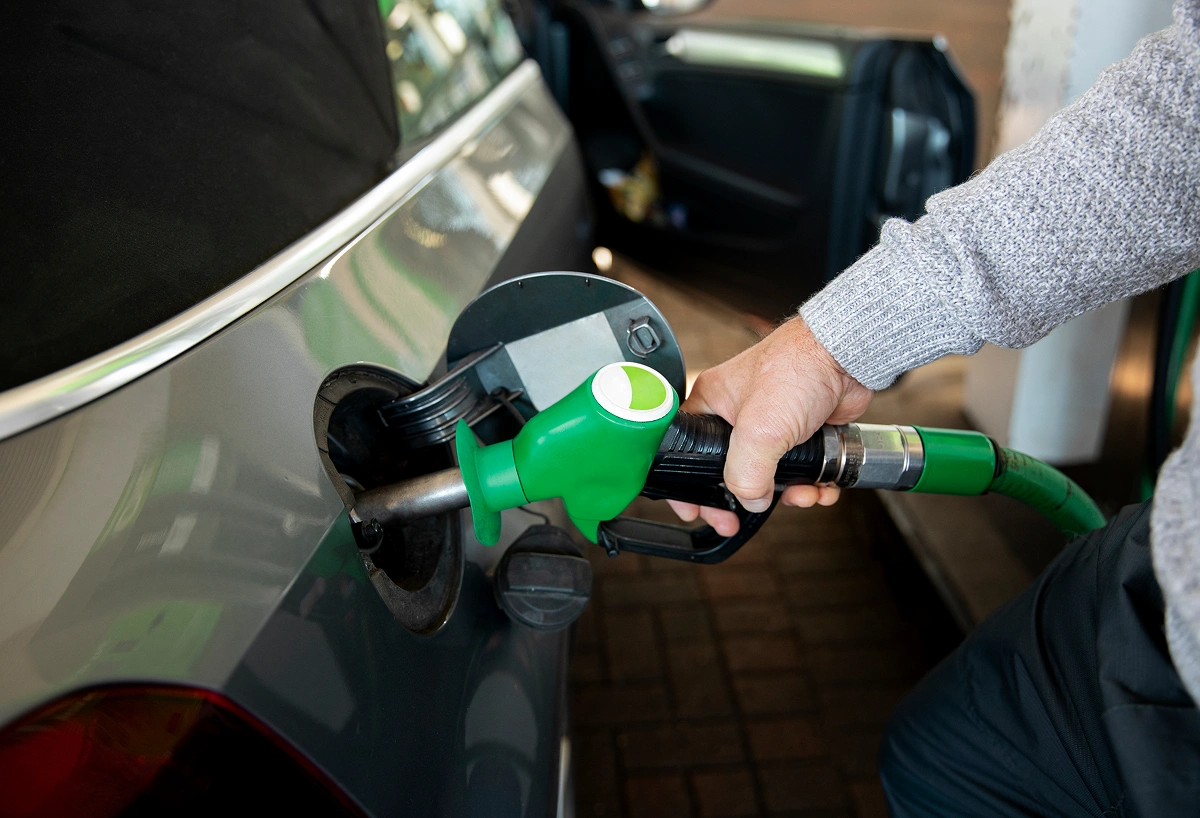 Person refueling a car with a green gasoline pump nozzle at a filling station.