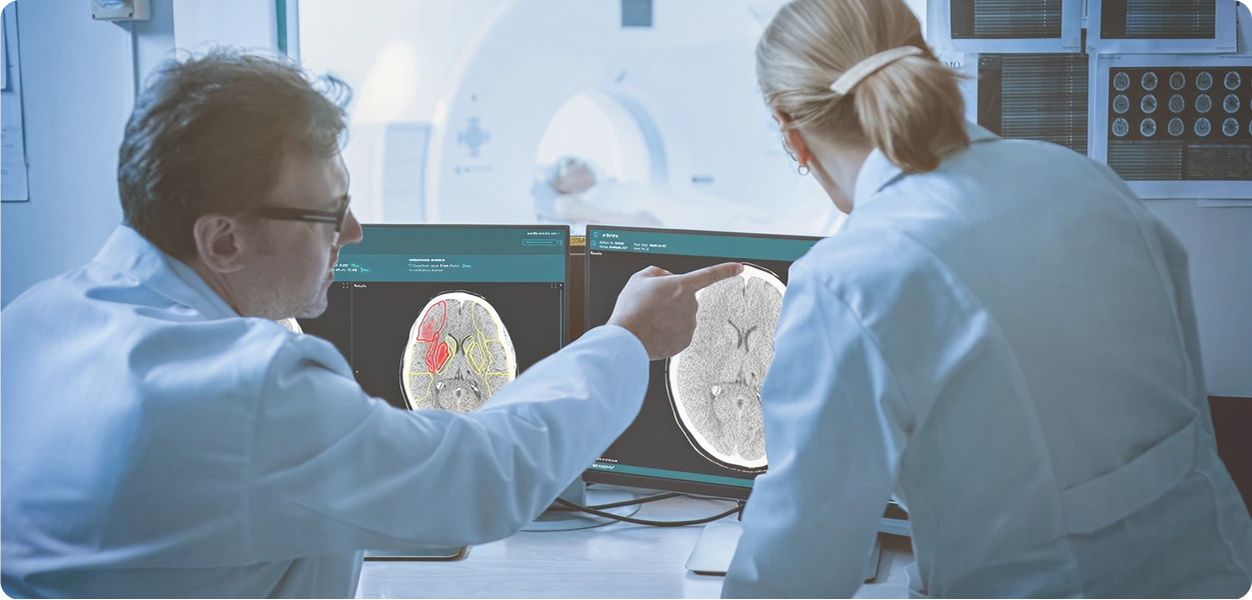 Two doctors examining brain scans on computer monitors in a medical imaging room.