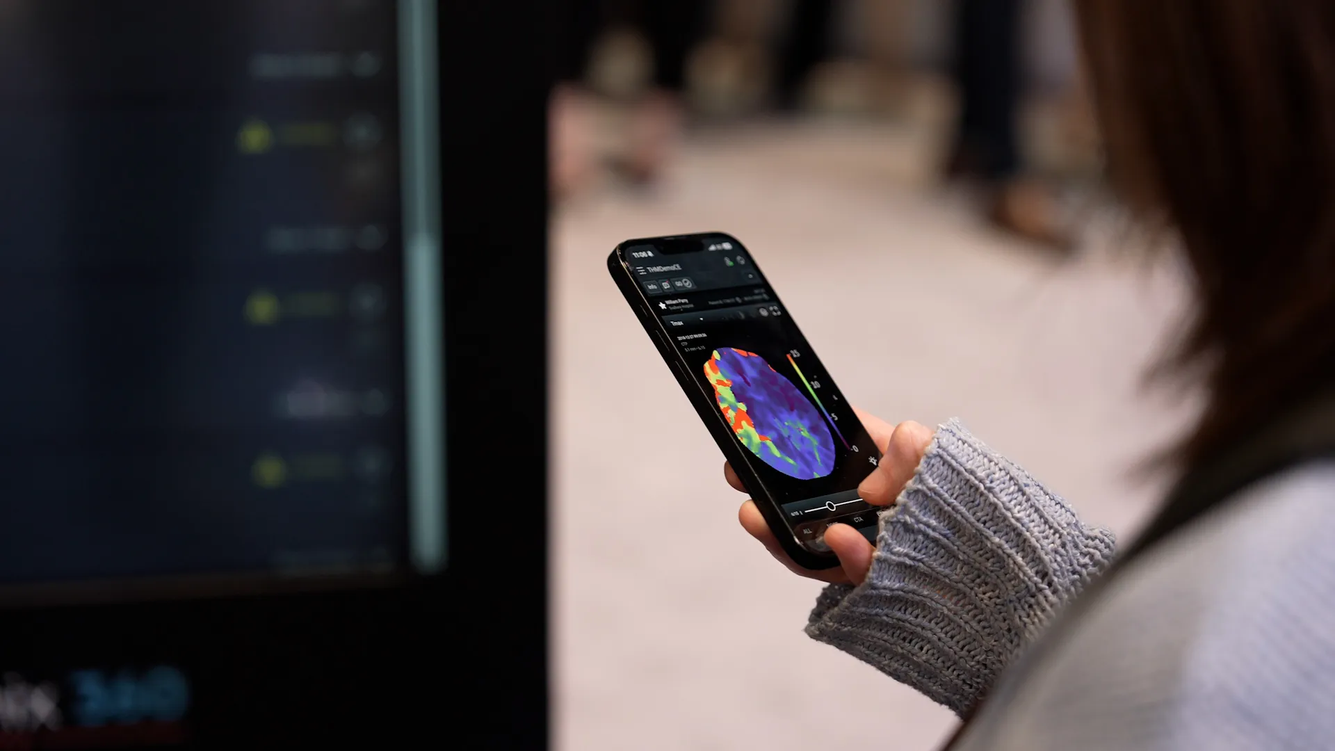 Person holding a smartphone displaying a colorful brain scan image with data controls.