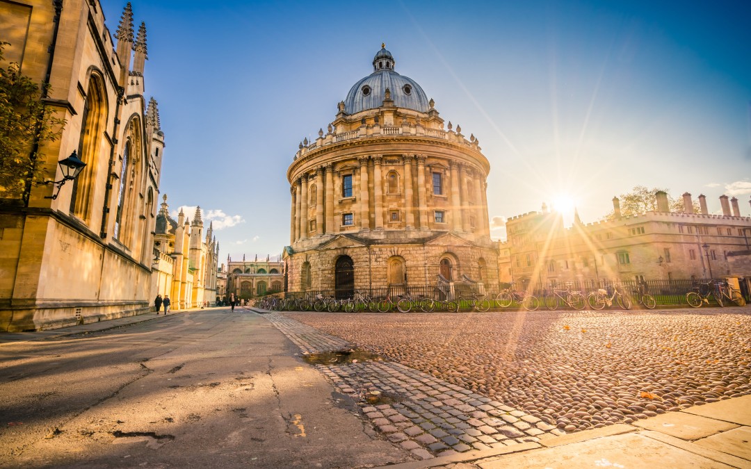 Radcliffe Camera building in Oxford with sun flare and historic buildings around it.