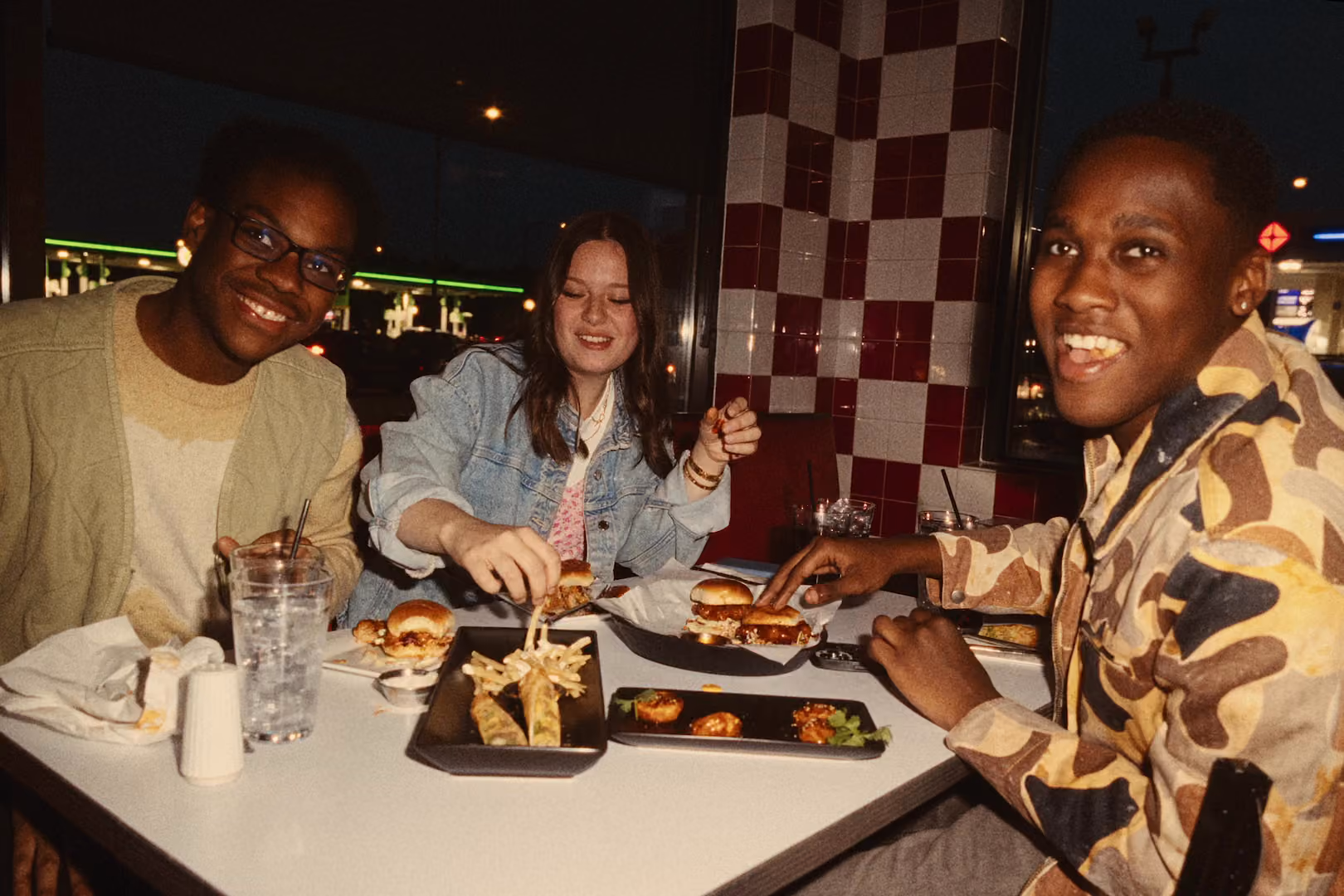 Three friends eating burgers around a table in a restaurant.
