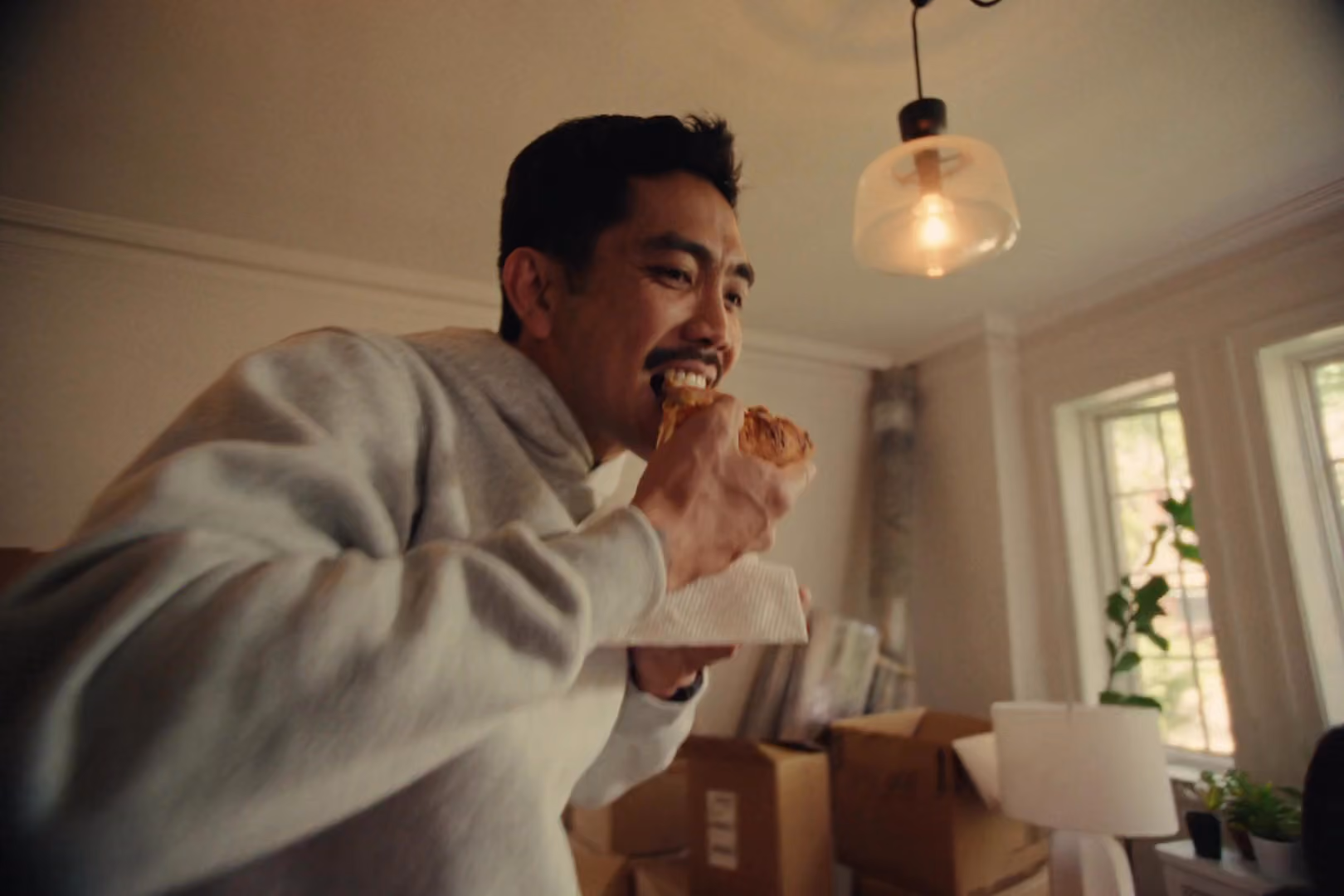 A man in a grey jumper eating pizza.
