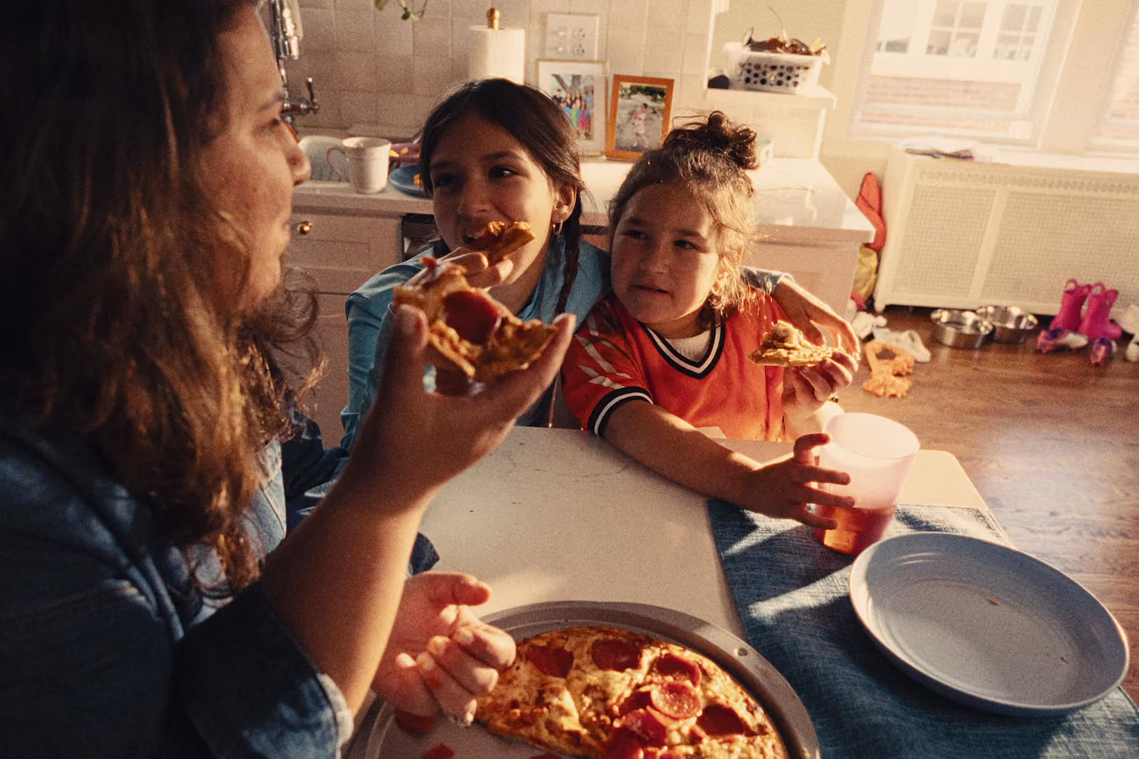 A woman and two girls eating pizza around a table.