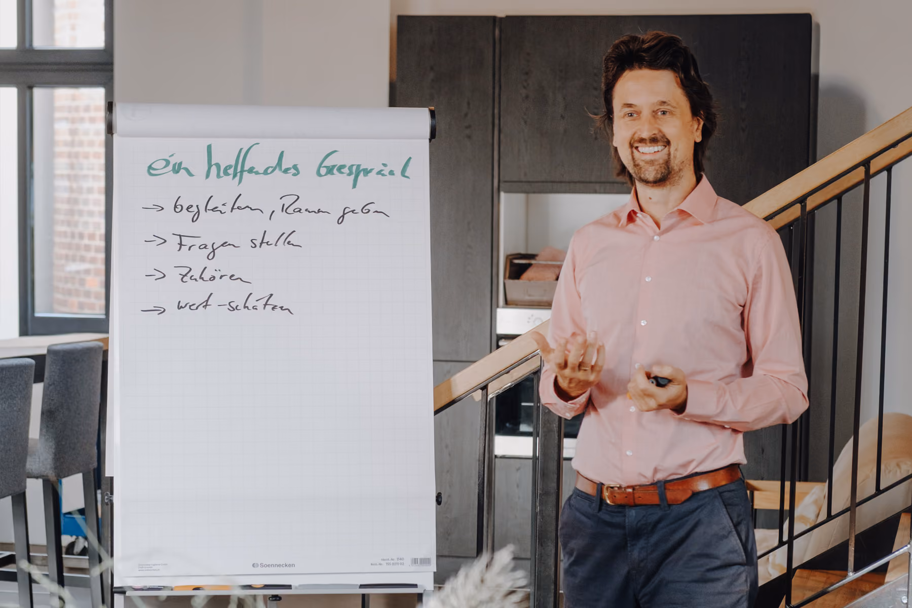 Dominik Frisch im rosa Hemd präsentiert Themen zu Transformation und Entwicklung am Flipchart im modernen Büro.