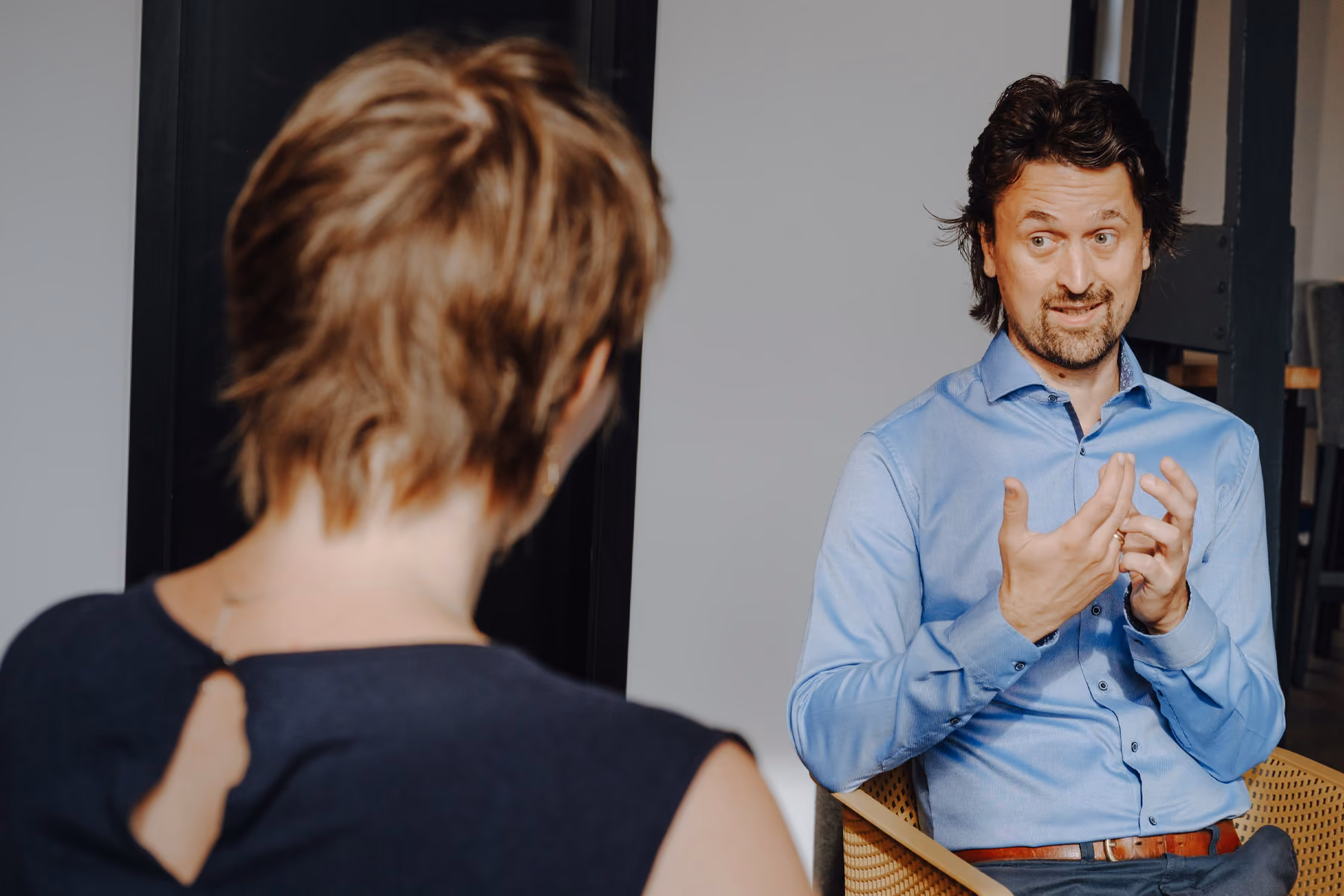 Dominik Frisch im hellblauen Hemd führt ein Gespräch mit einer aufmerksam zuhörenden Frau im Büro.