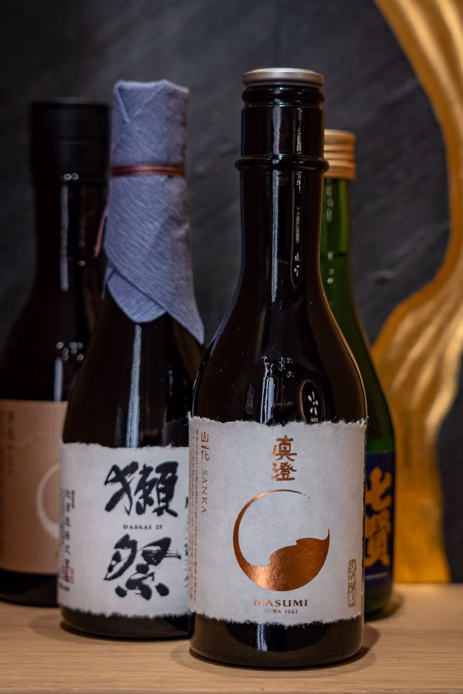 Vier besondere japanische Sakeflaschen mit Etiketten, die japanische Schriftzeichen zeigen auf einer Holzoberfläche im Nashi Dining im Zentrum von Erfurt