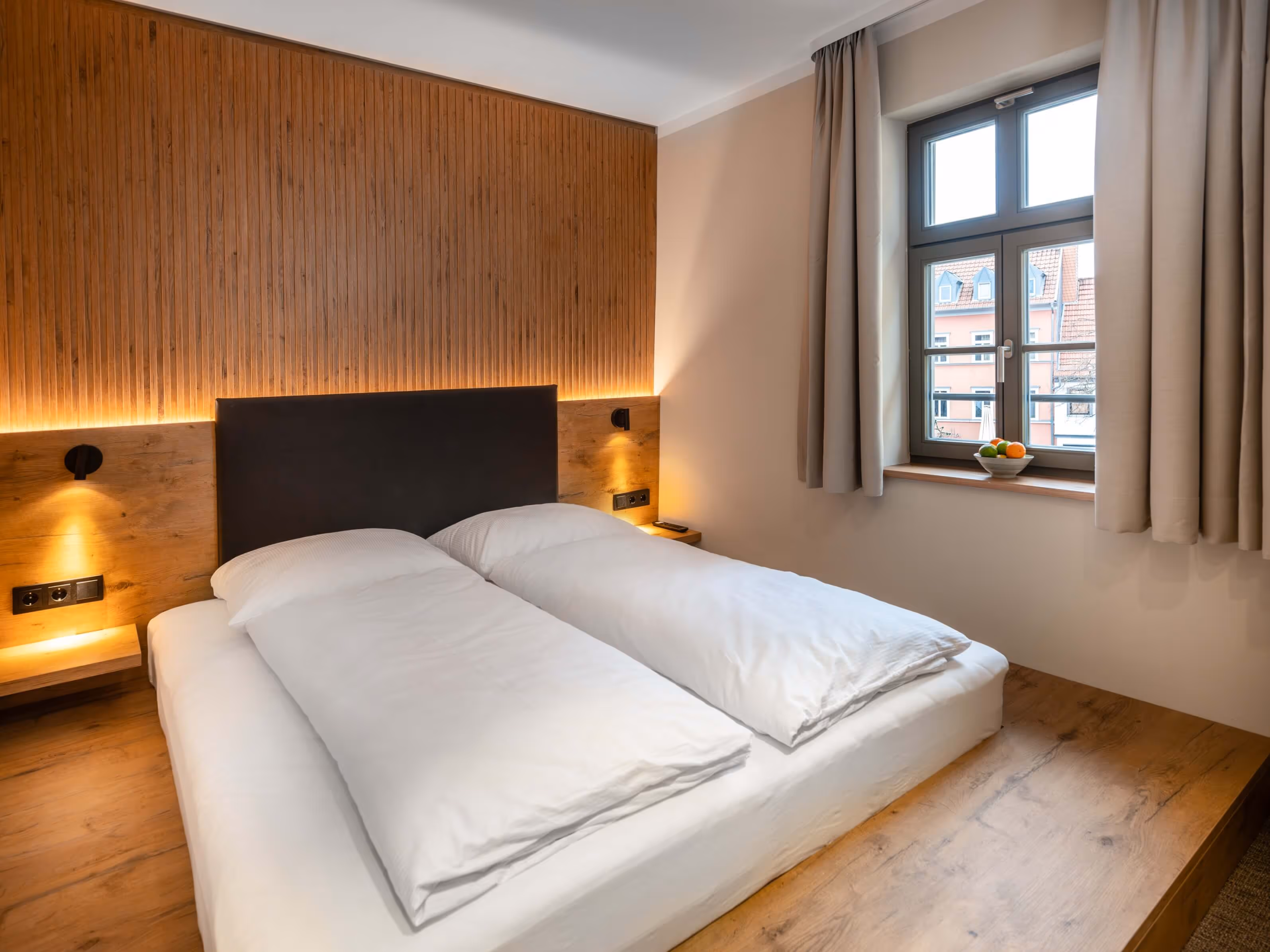 Nashi Rooms Hotel, modern Japanese-style bedroom with futon bed, wood-paneled accent wall and window with views over the rooftops of Erfurt's old town.