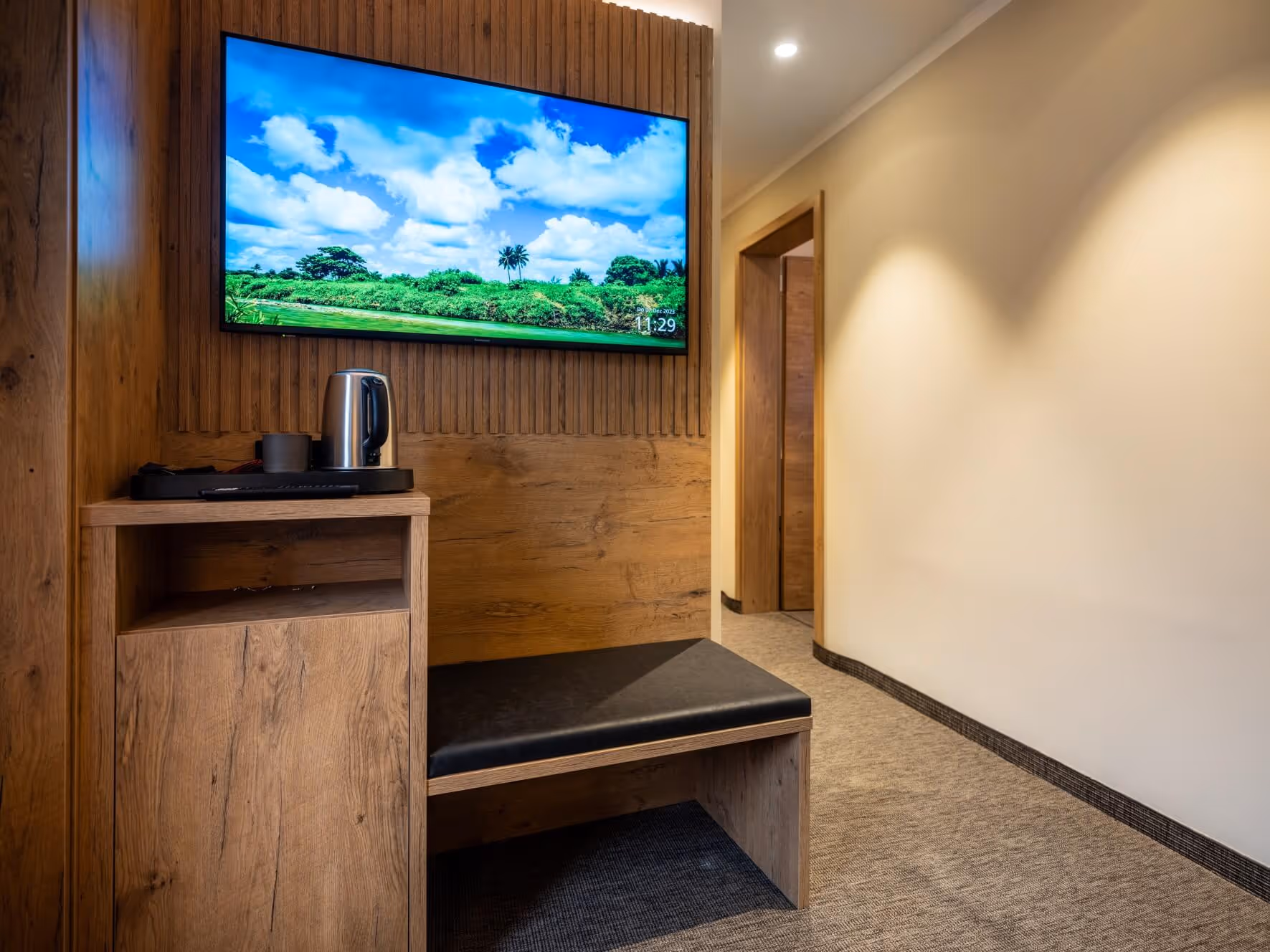Hotelzimmerecke mit Holzvertäfelung, einer Bank, einem Wasserkocher auf einem Holzregal und einem Flachbildfernseher, im Nashi Rooms Hotel in Erfurt nahe der Krämerbrücke.