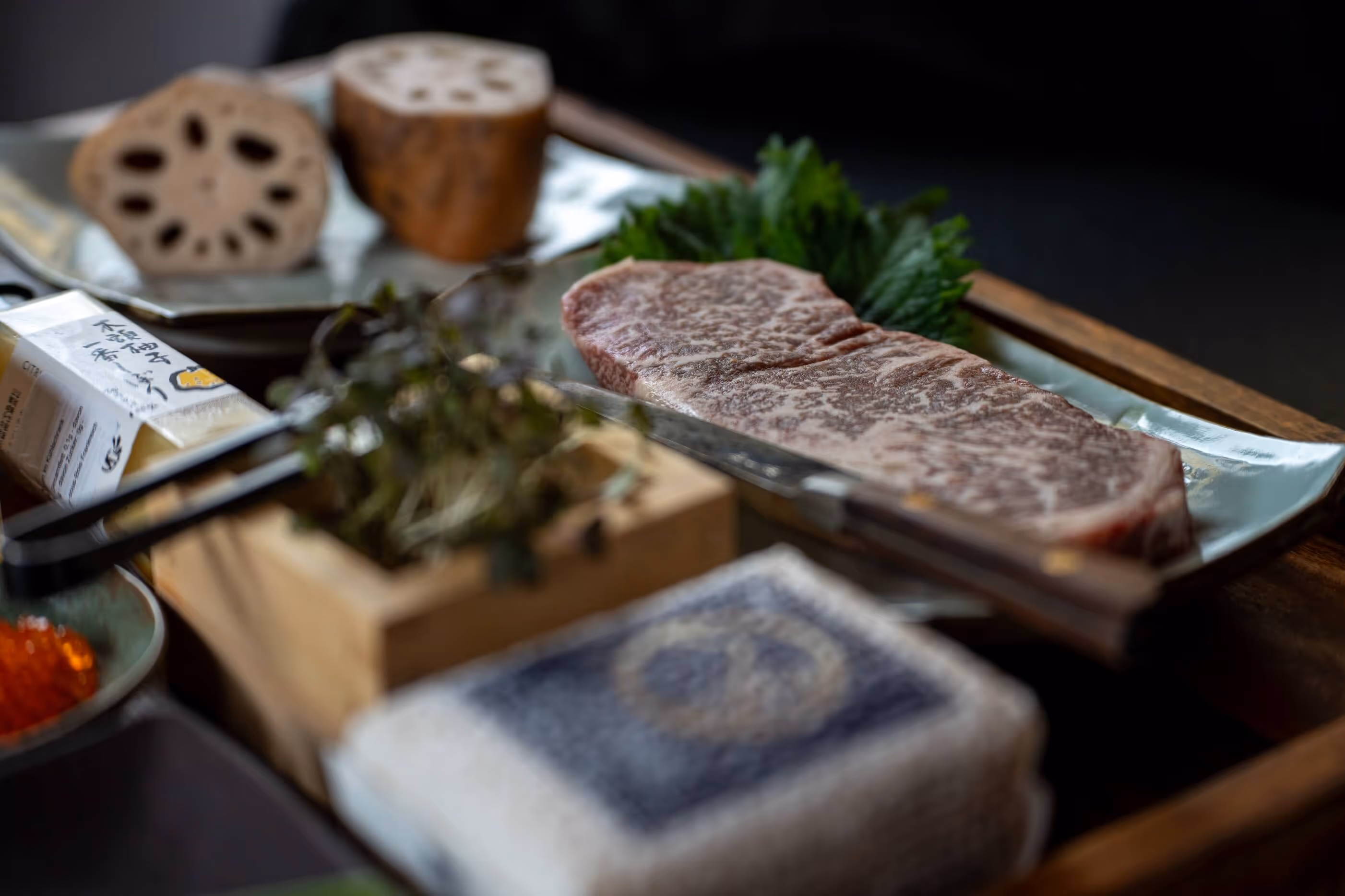 High-quality raw meat on a plate with green leaves, plus lotus root slices, herbs and a spice pack on a wooden tray at Nashi Dining in Erfurt.