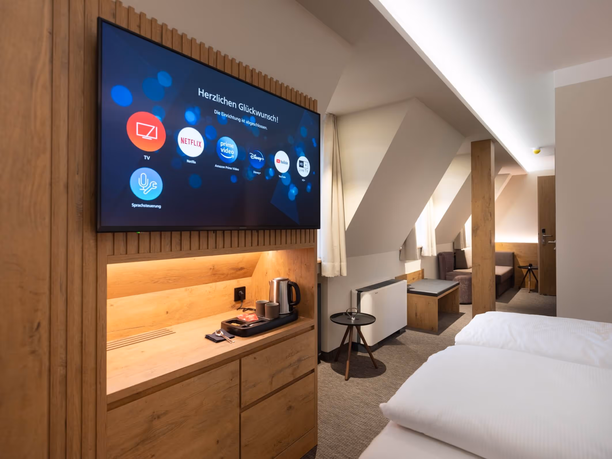 Modernes Hotelzimmer mit Holzmöbeln, Fernseher mit Streaming-Apps, Doppelbett und Schlafcouch im Nashi Rooms Hotel an der Krämerbrücke in Erfurt.