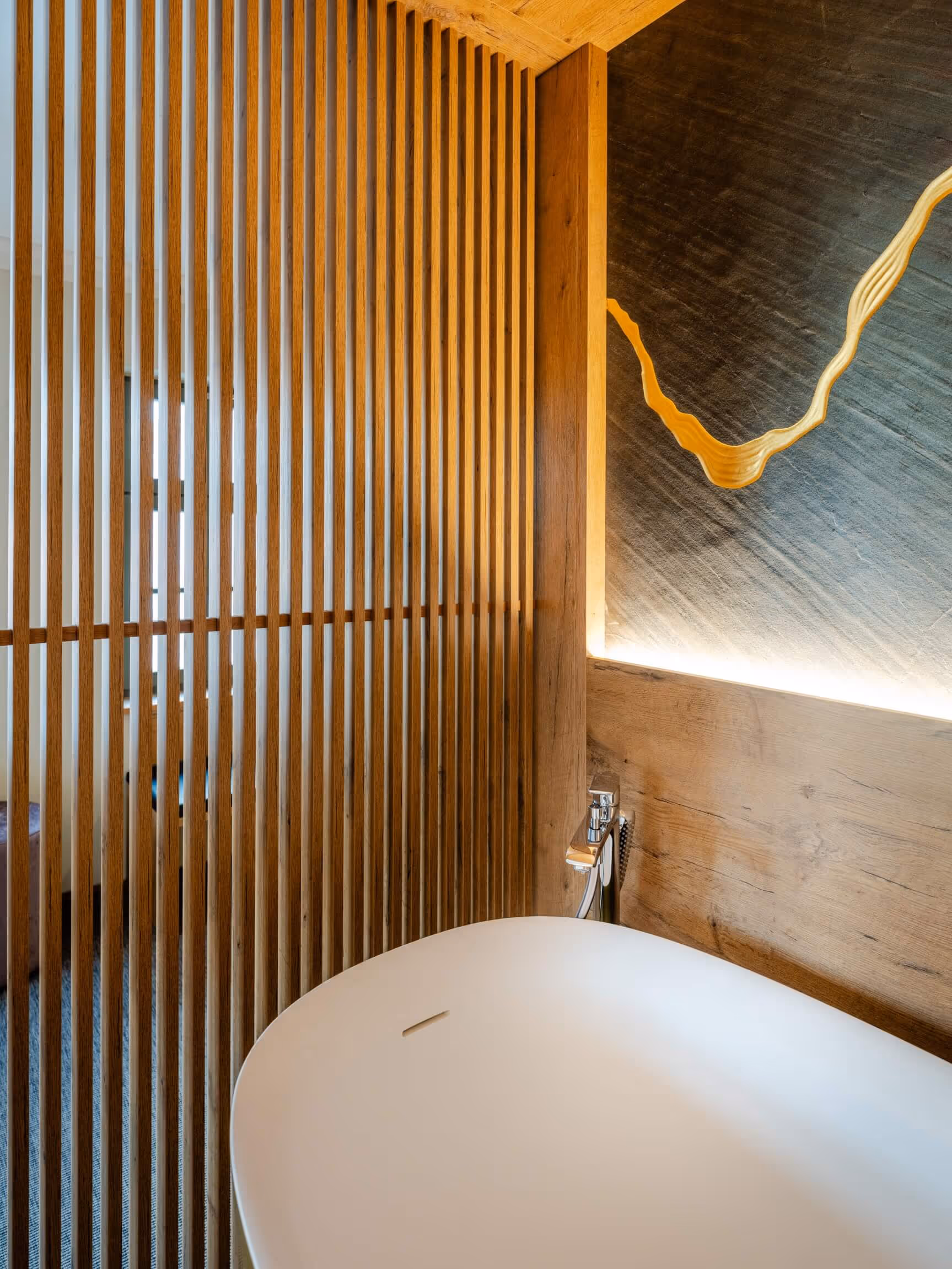 Moderne Badewanne vor einer Holzlamellenwand und beleuchteter Wand im Nashi Rooms Hotel im Zentrum von Erfurt.