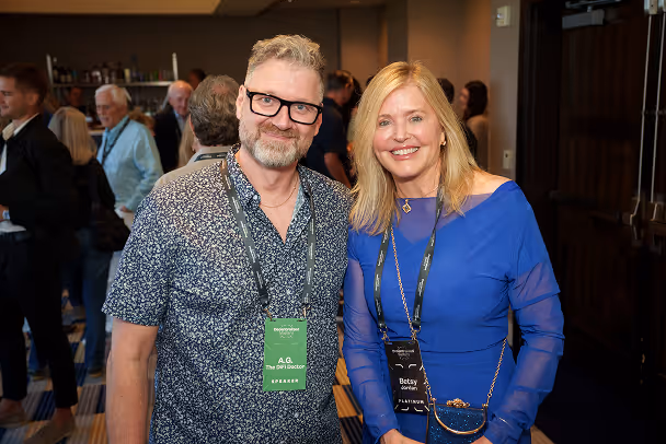 Speaker and attendee posing together at networking reception, event hall with guests in background