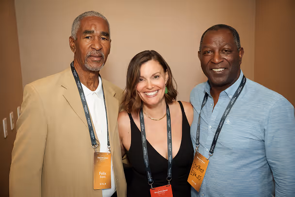 Three attendees posing together with lanyards, smiling at networking event