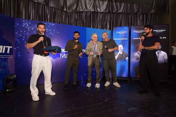 Award presentation on stage with four participants in front of Decentralized Masters LED backdrop at event