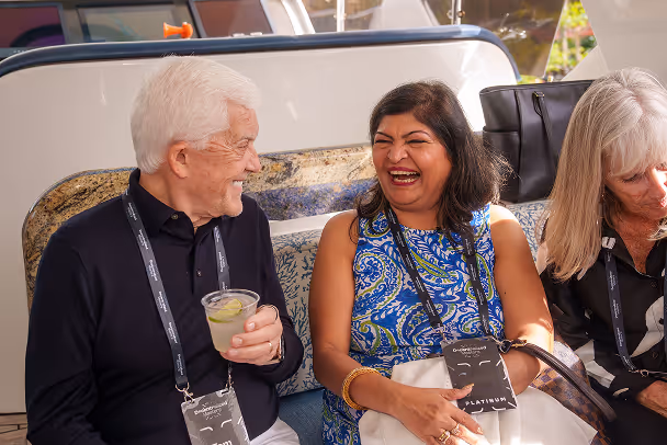 Three attendees laughing and socializing inside yacht cabin, holding drinks with lanyards visible