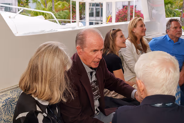 Attendees seated in intimate conversation on yacht deck, tropical marina setting in background