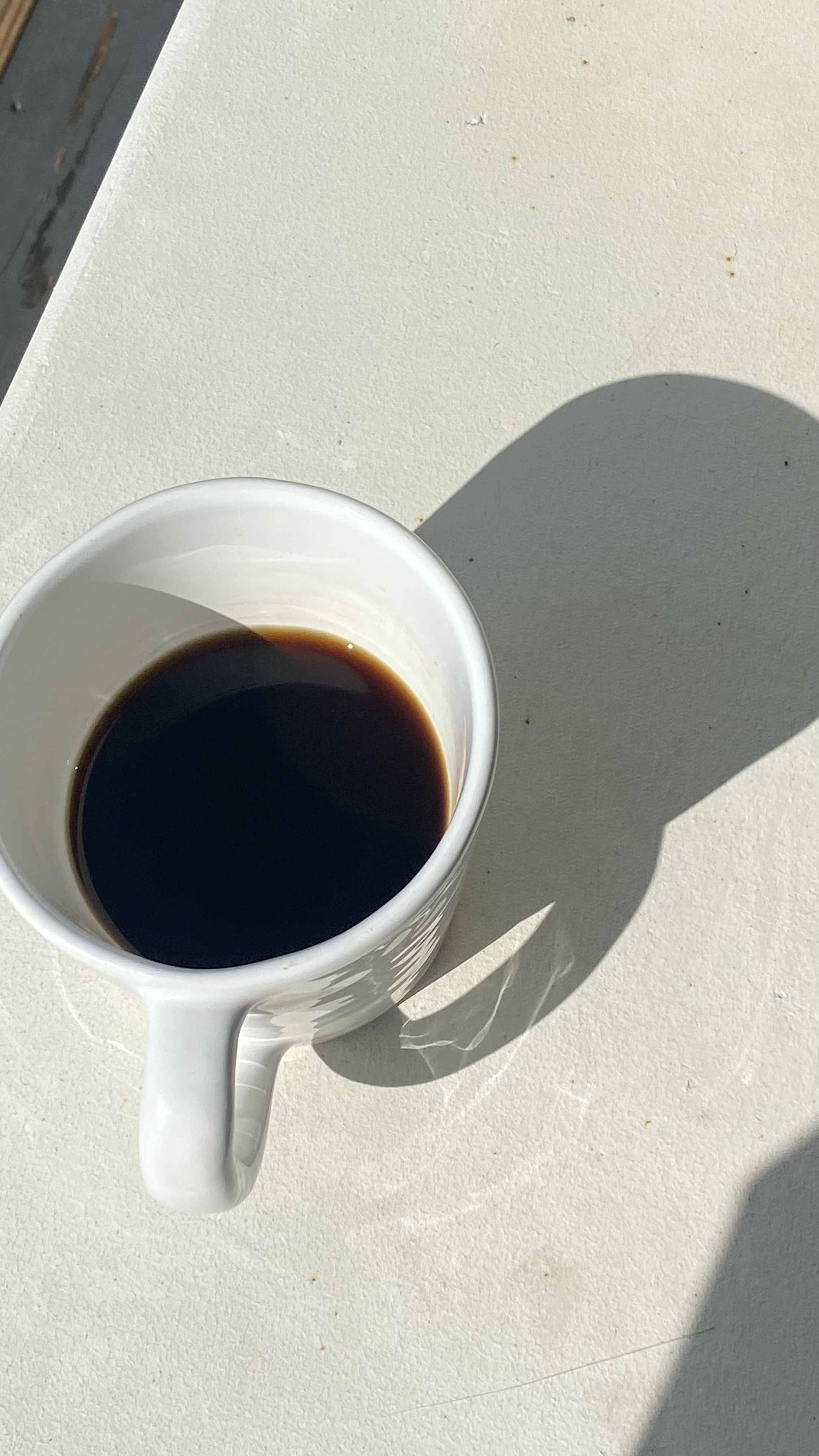 White ceramic mug with black coffee casting a shadow on a textured light surface.