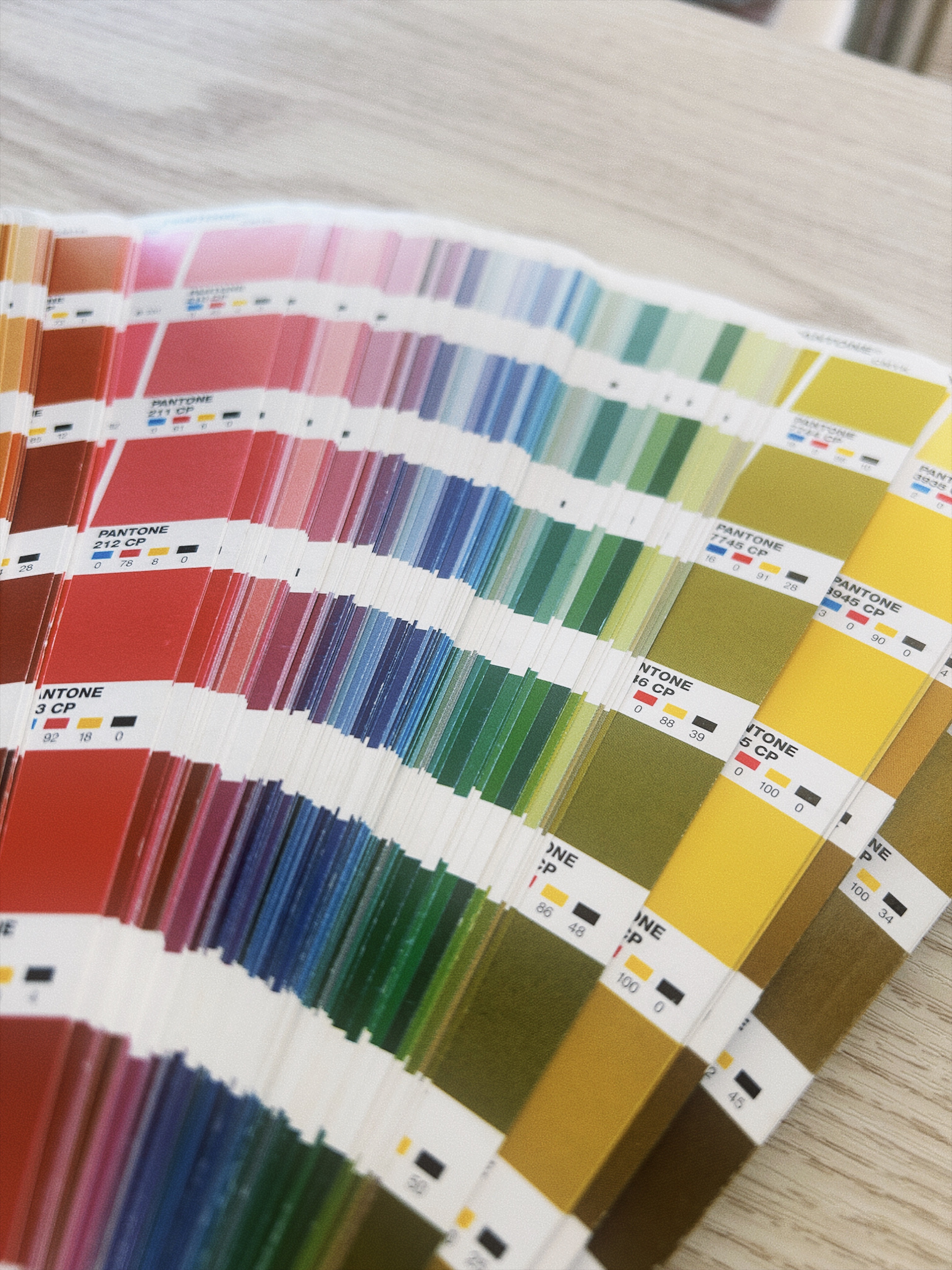Open Pantone color swatch book showing a range of colors organized by shade on a wood surface.