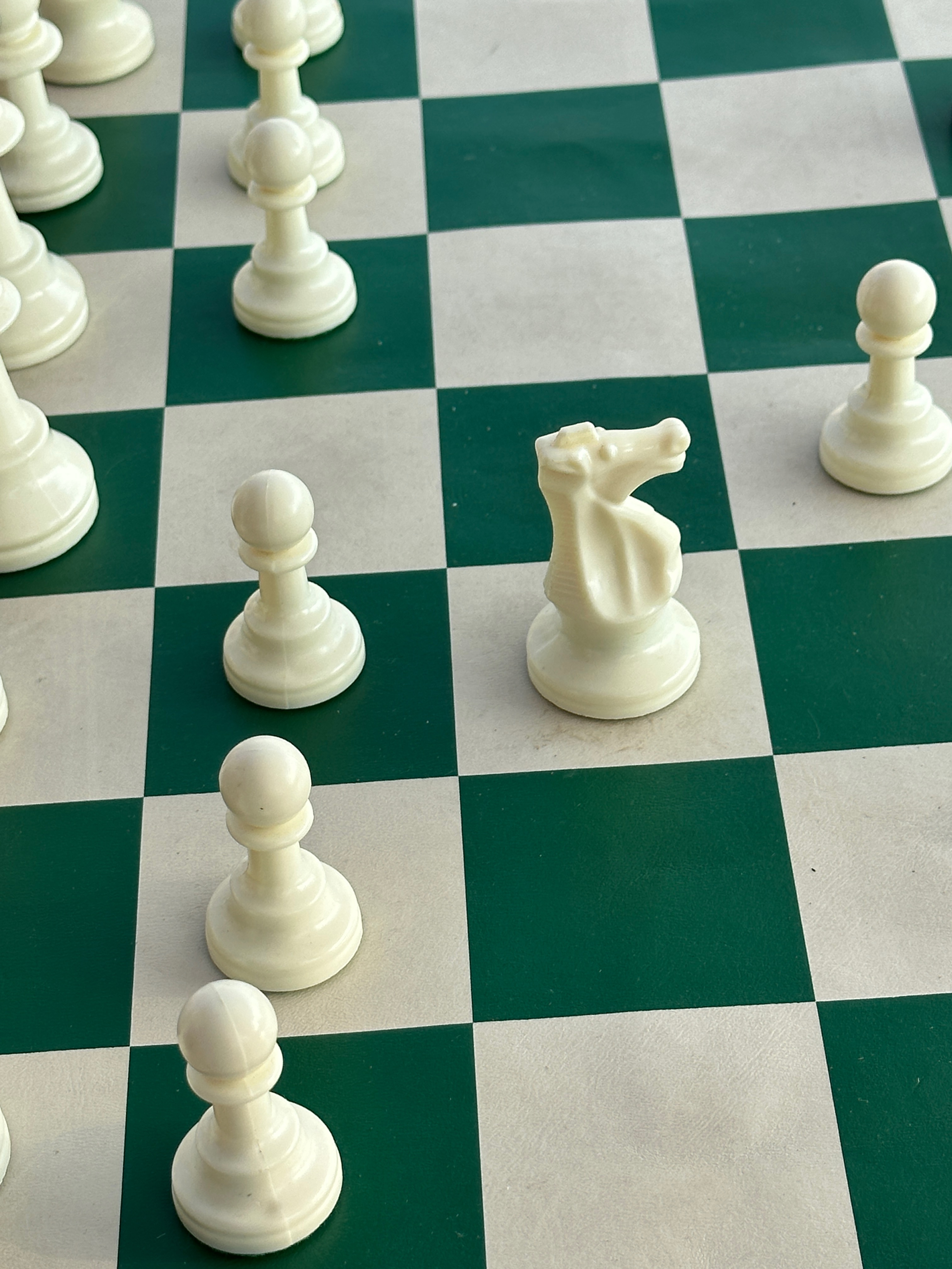 White chess pieces including a knight and pawns on a green and white chessboard.