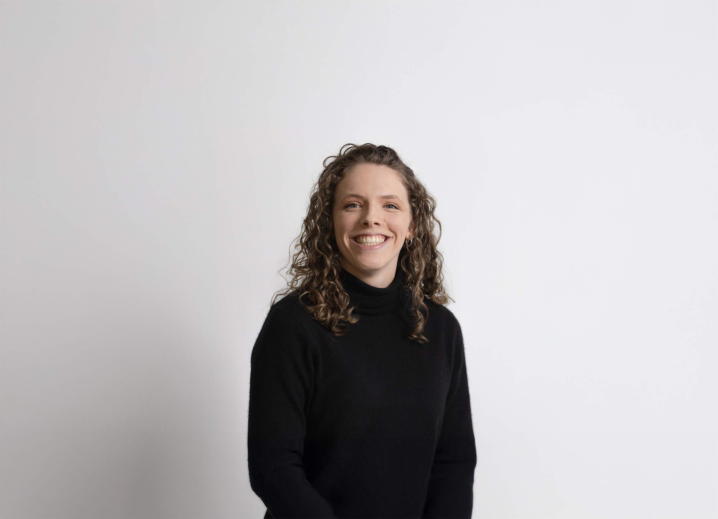 Smiling woman with curly hair wearing a black turtleneck sweater against a plain white background.
