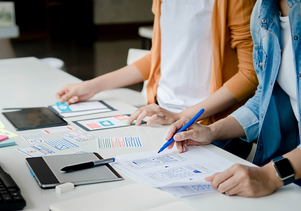 Two people working on app design sketches and user interface layouts at a white table.
