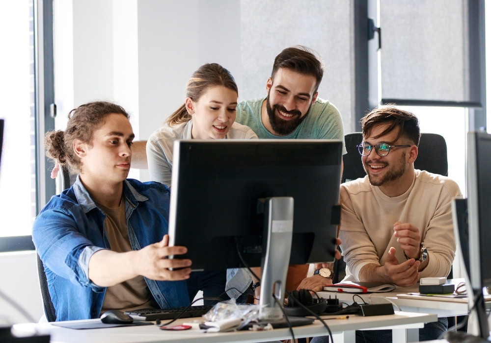 Four young adults collaborating around a computer in a bright modern office.