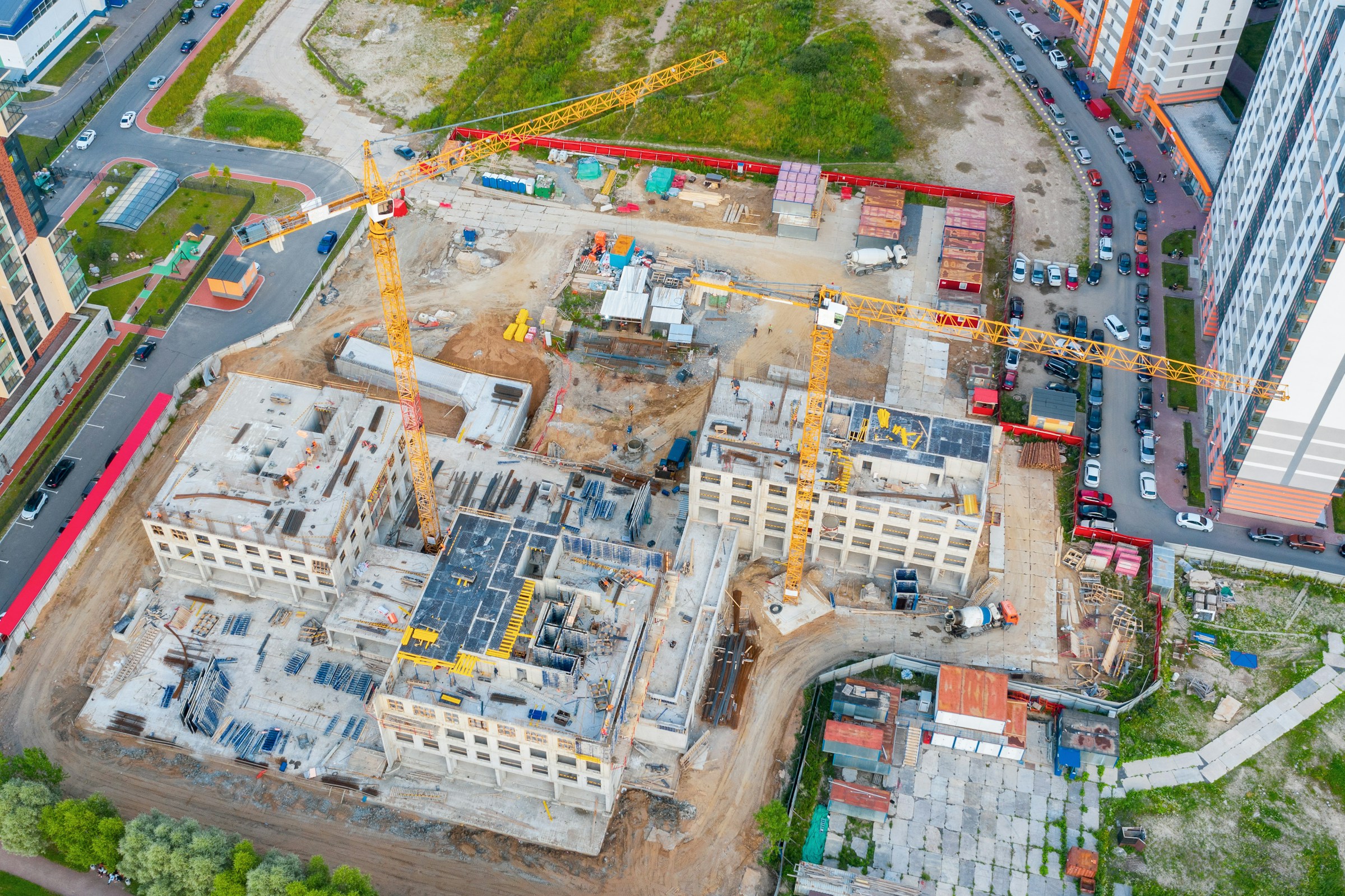 Luchtfoto van een bouwplaats met twee grote hijskranen en gebouwen in aanbouw.