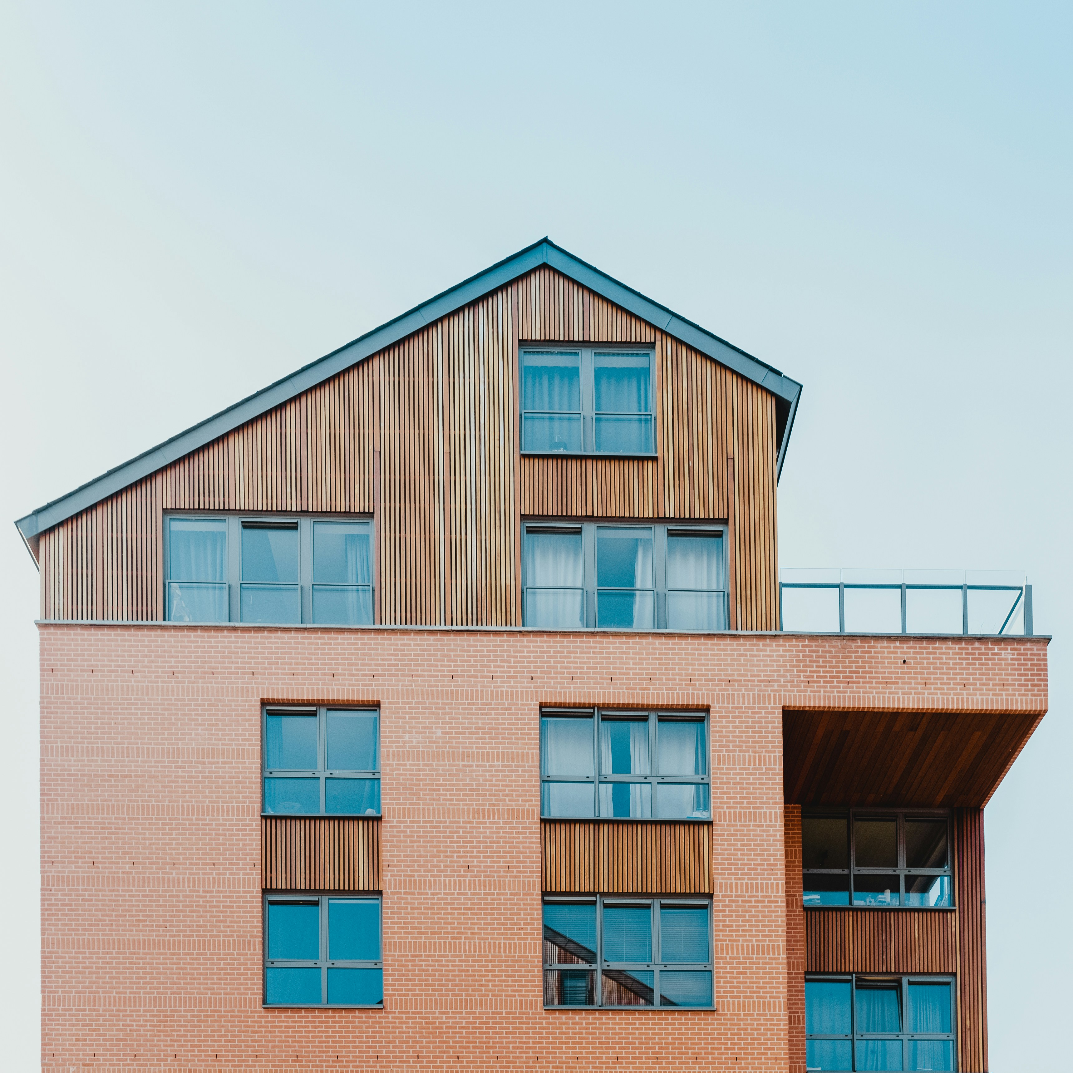 Moderne woning met bakstenen en houten gevels en grote ramen onder een blauwe lucht.